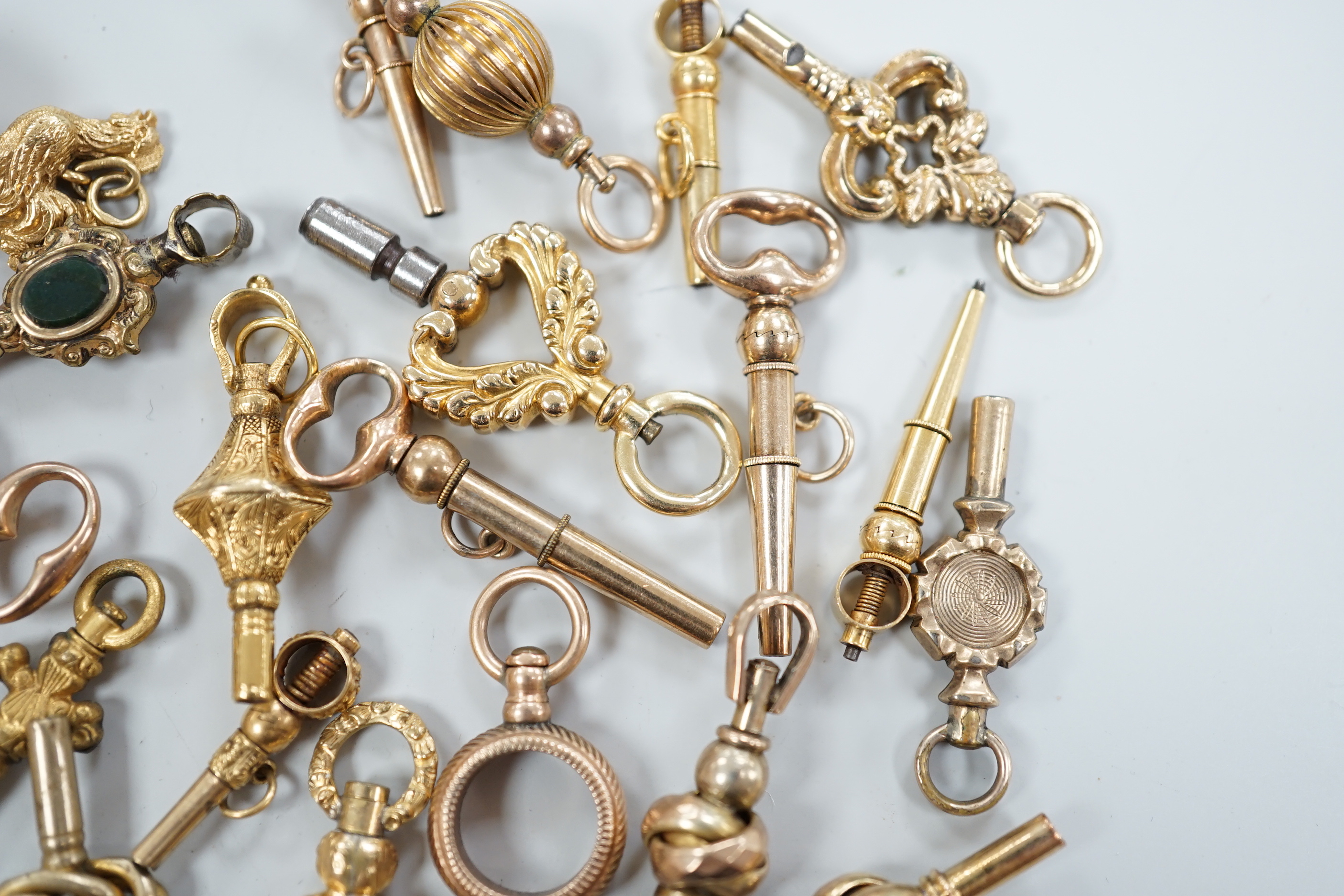 Twenty assorted mainly 19th century yellow metal small watch keys, including trade insignia, bloodstone set and keys to be turned in one direction, largest 37mm, together with a 19th century yellow metal overlaid and aga